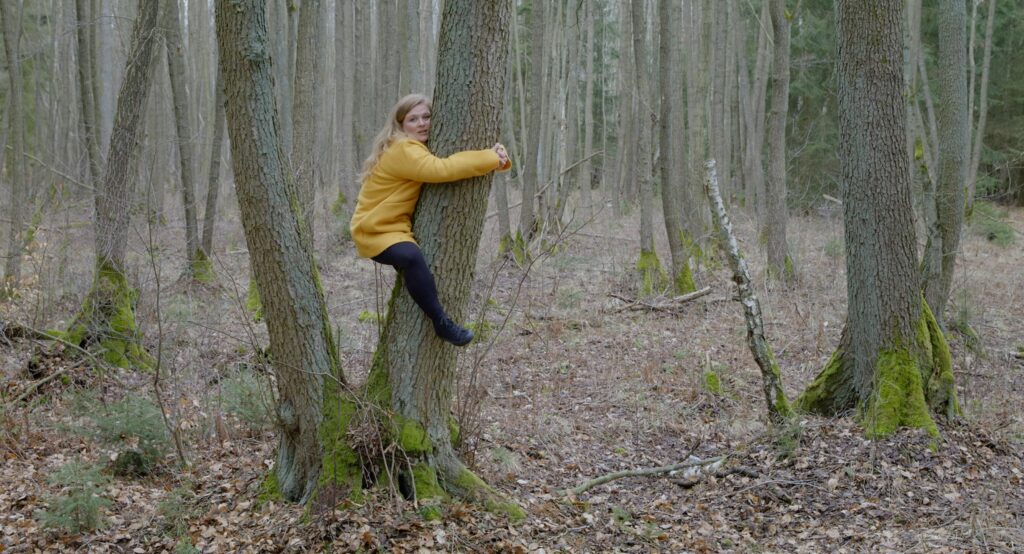 eine Schauspielerin ist an einen Baumstamm geklammert in zwei Metern Höhe