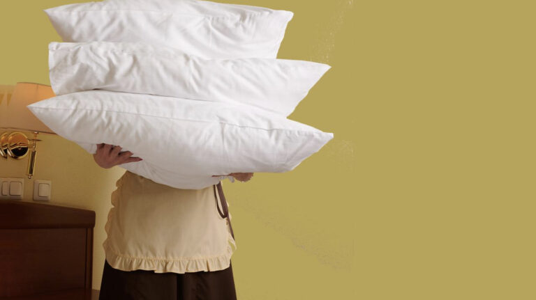 A person wearing an apron holds three pillows in front of their body